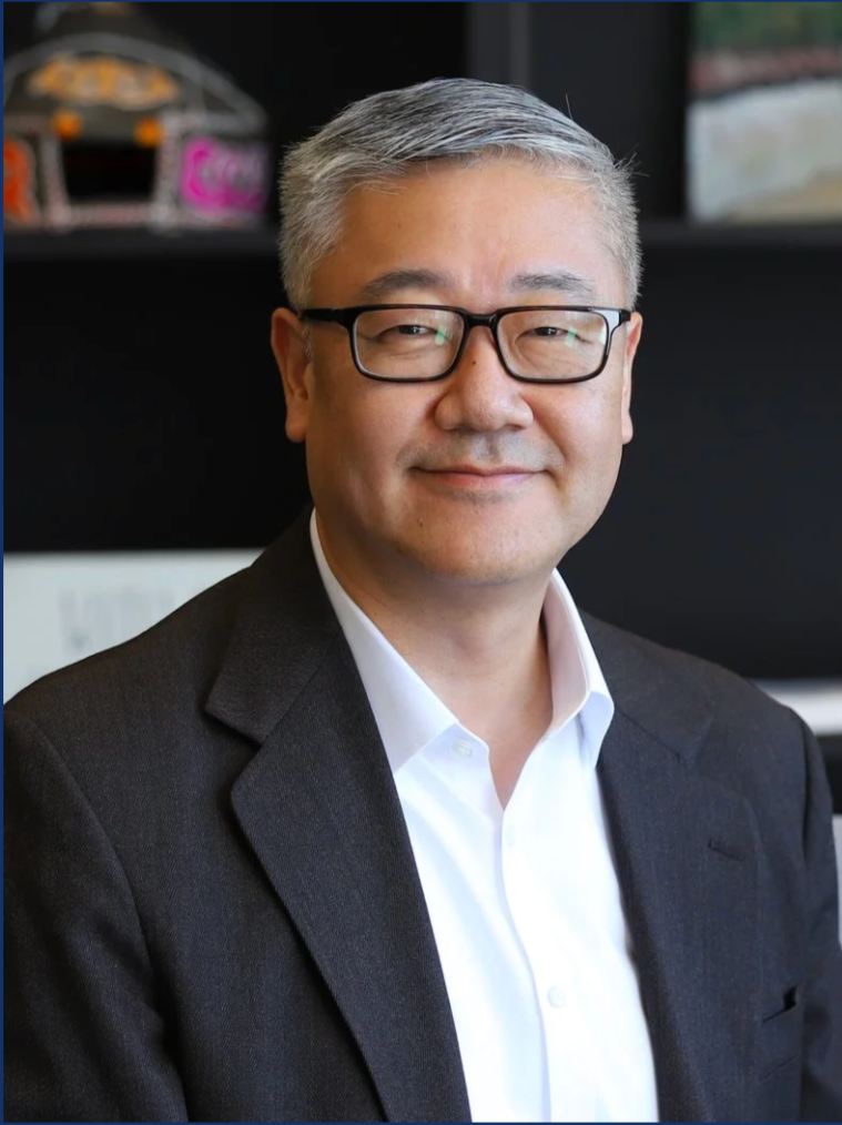 A Korean man with grey hair wearing a blazer, a white shirt and glasses.