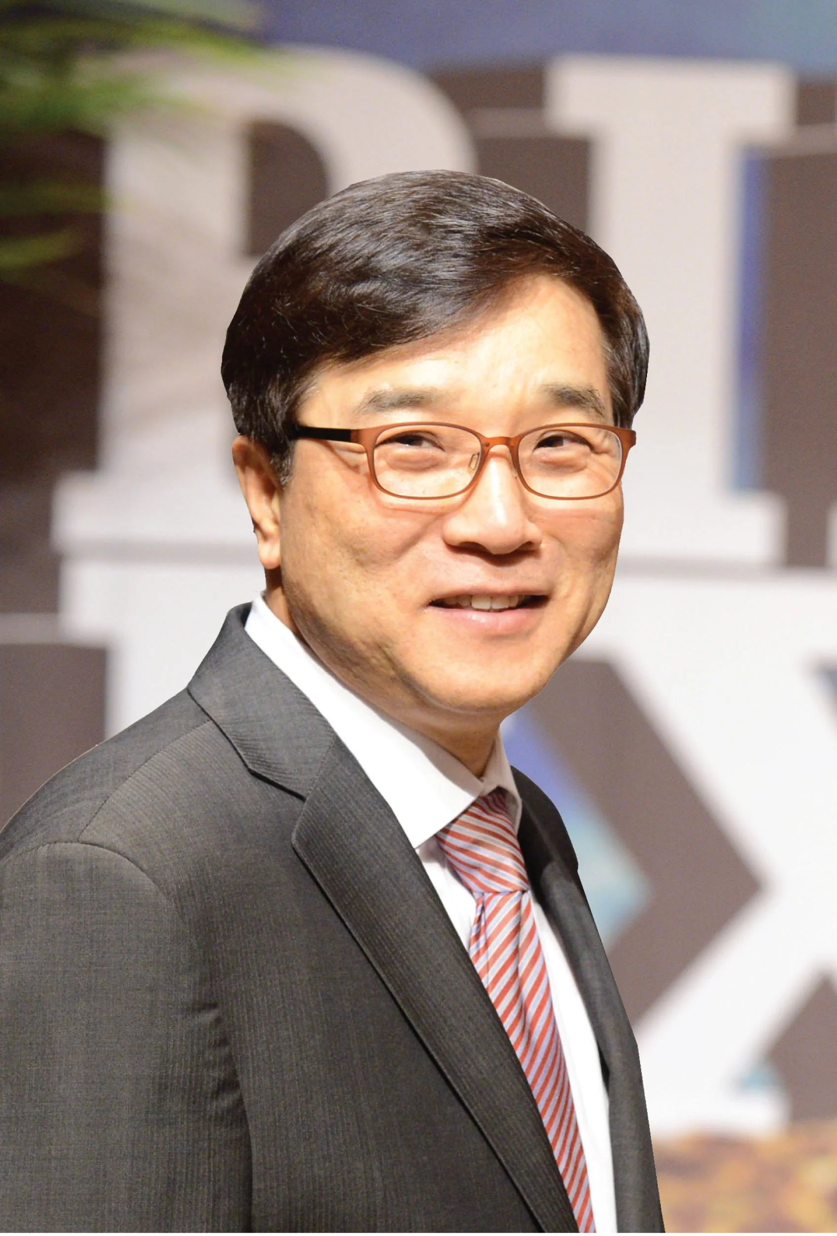 A man in a gray suit, white shirt, red striped tie, and glasses smiling at an event.