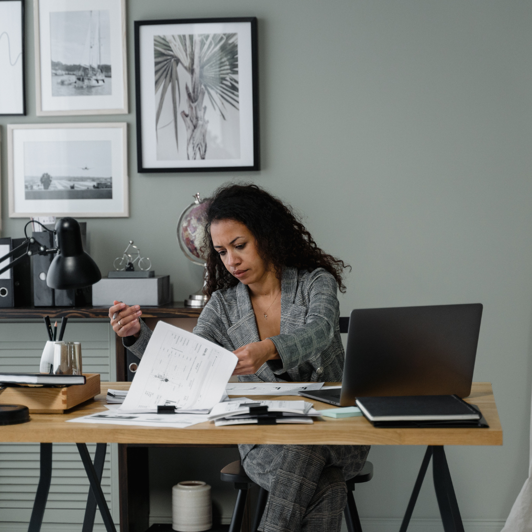 business woman in plaid blazer sitting at a table reviewing documents and a laptop