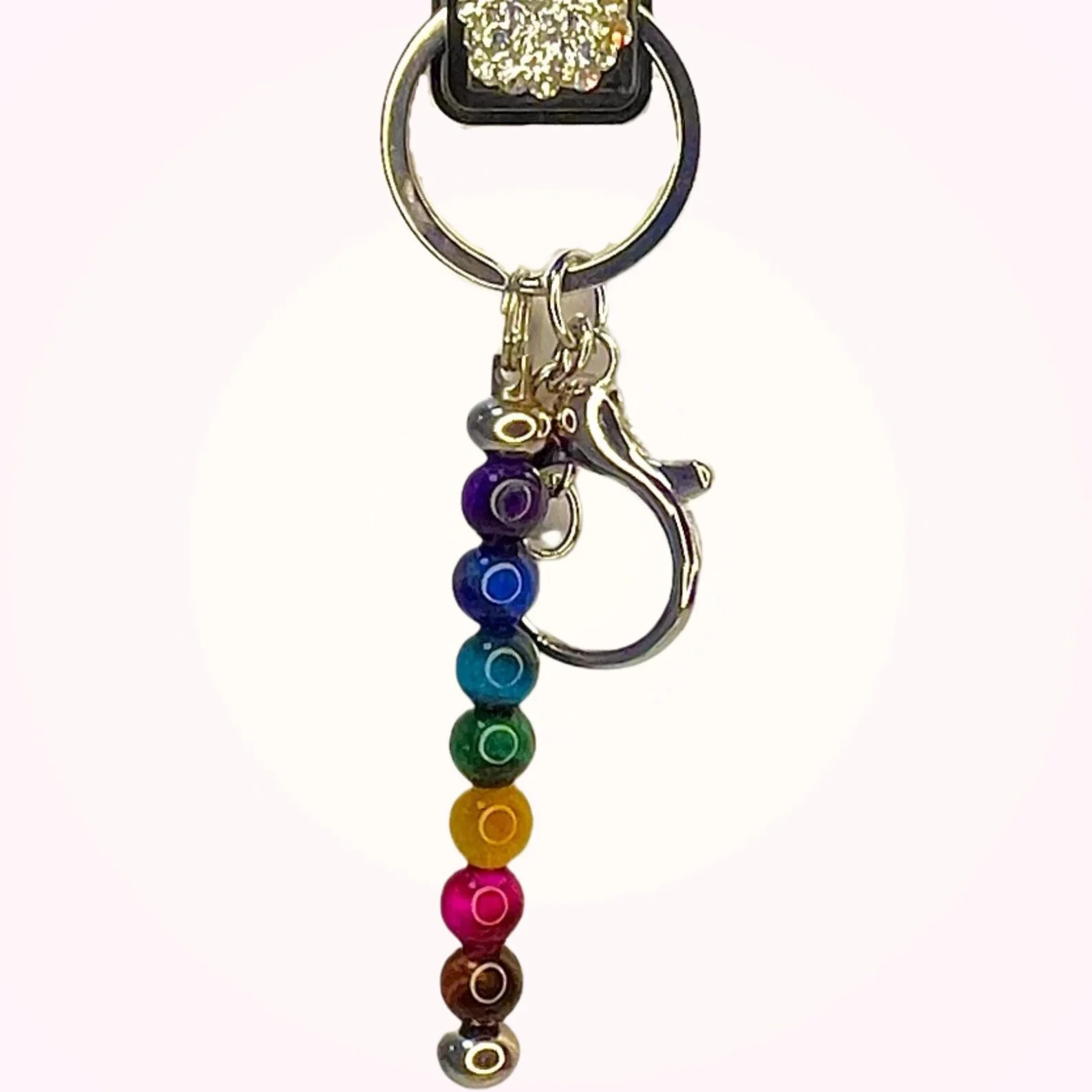 chakra keychain with seven stacked rainbow beads and a silver clasp, photographed on a pale pink background.