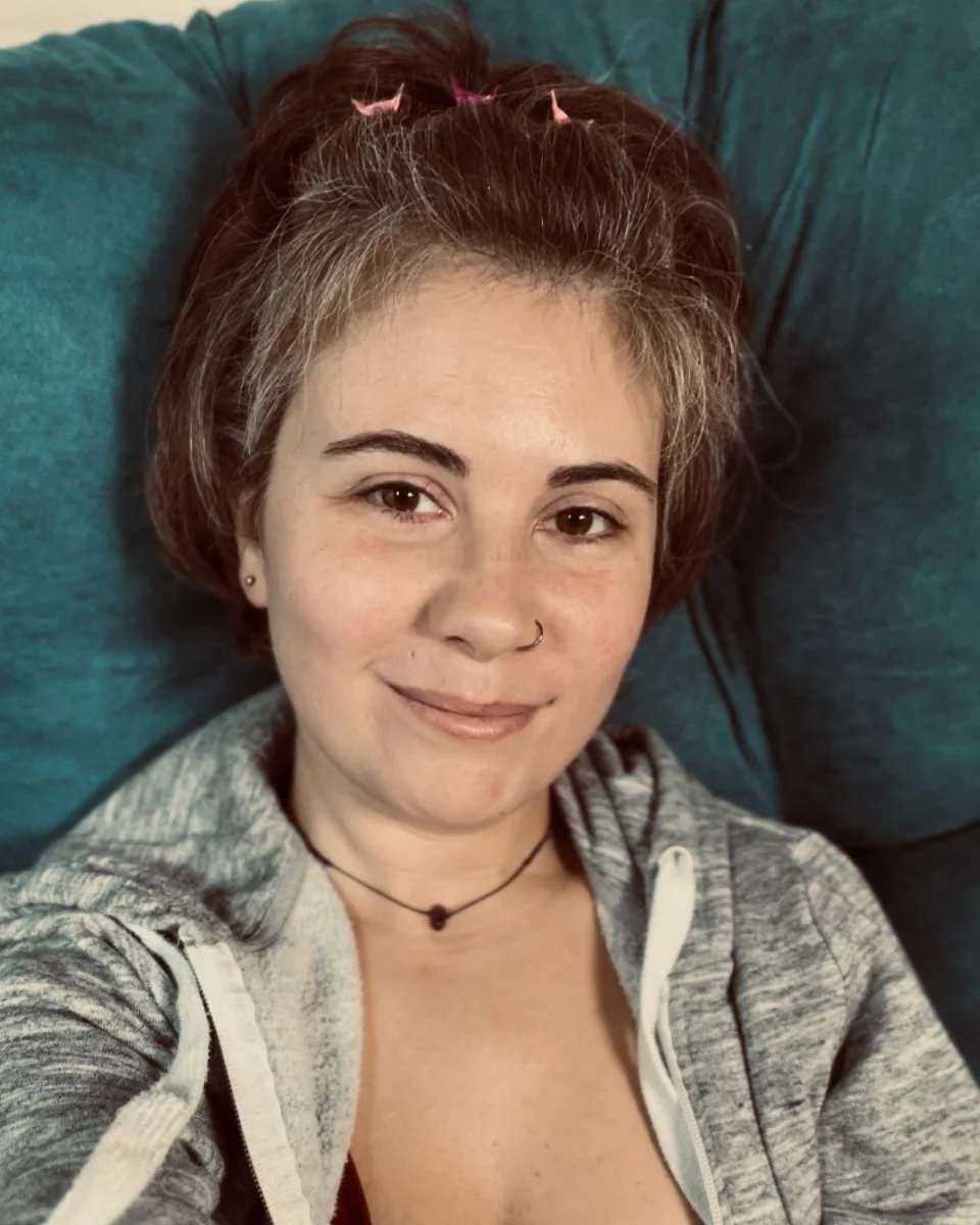woman with short reddish-brown hair lying on a teal pillow, smiling slightly at the camera in soft lighting