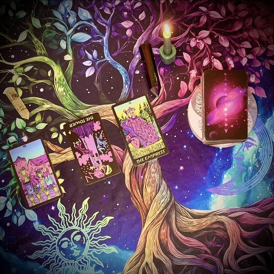 three tarot cards laid out face up in a loose spread, with the rest of the deck face down beside them on a vibrant, tree-patterned cloth featuring swirling stars and psychedelic designs