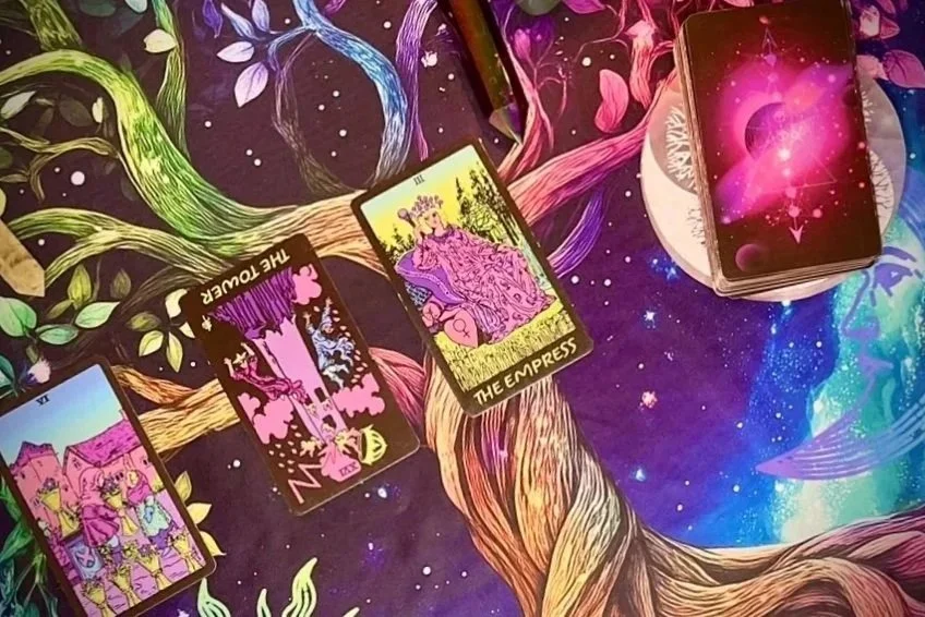 three tarot cards laid out face up in a loose spread, with the rest of the deck face down beside them on a vibrant, tree-patterned cloth featuring swirling stars and psychedelic designs