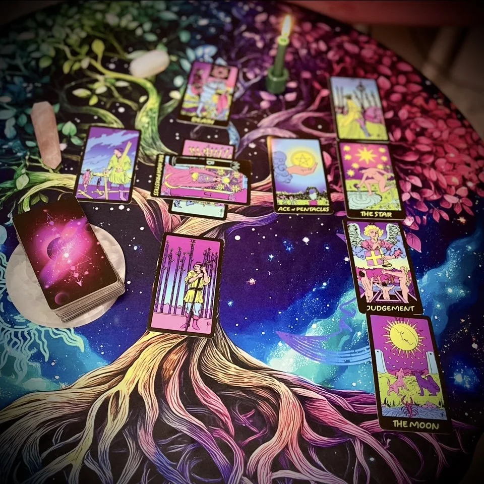 several tarot cards laid out face up on a vibrant, cosmic-patterned cloth, featuring bold colors and galactic imagery. visible cards include the star, ace of pentacles, and judgment. the deck sits off to the left.