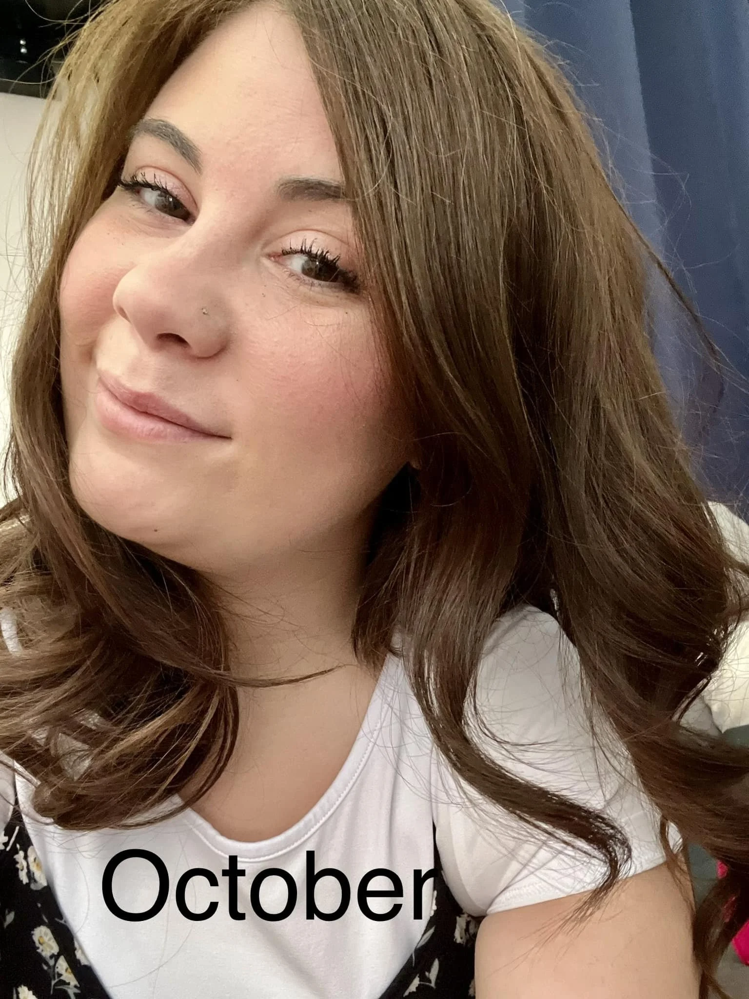 woman with long wavy light brown hair smiling, with "October" overlaid in black text on a white shirt