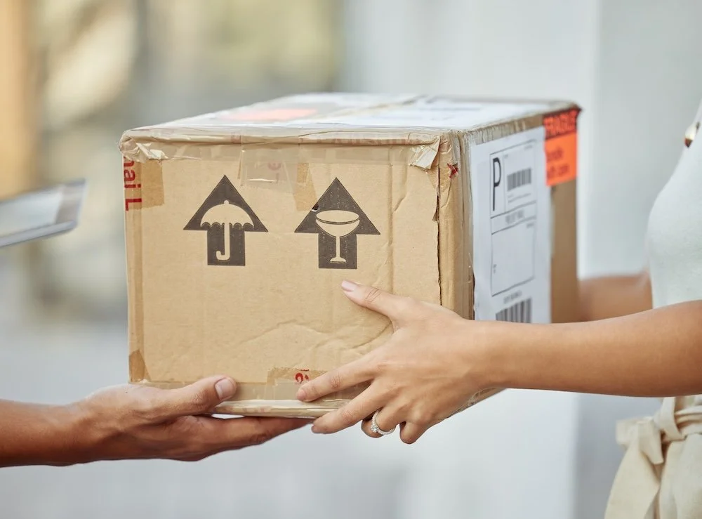 Two people exchanging a cardboard box, with symbols indicating this may contain fragile or handle with care items.