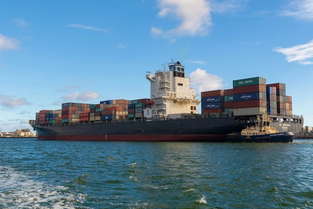 A cargo ship carrying numerous stacked shipping containers in a harbor.