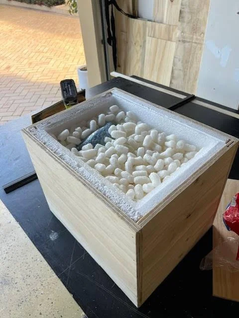A wooden display freezer filled with white packing peanuts and a tablet or small device inside.