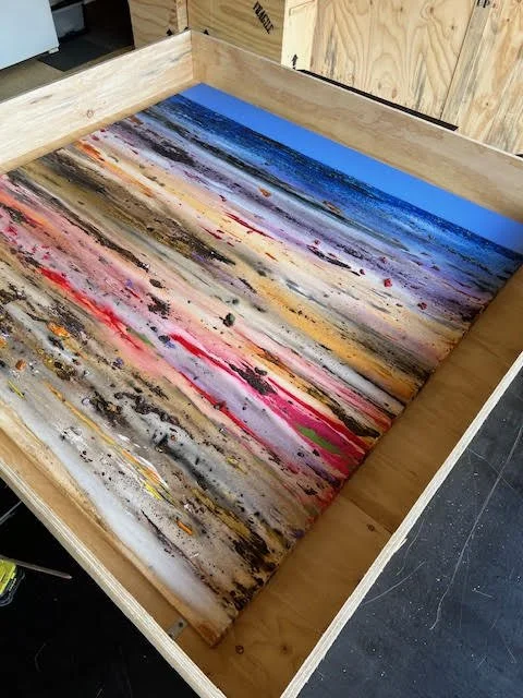 A large wooden box with a colorful abstract painting on the inside bottom, featuring streaks of blue, pink, black, beige, and orange.