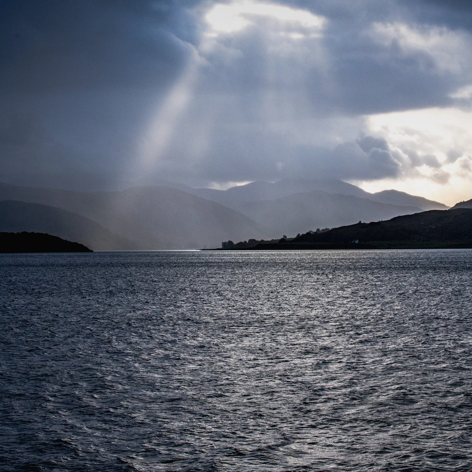 A river with mountains in the background under a cloudy sky.