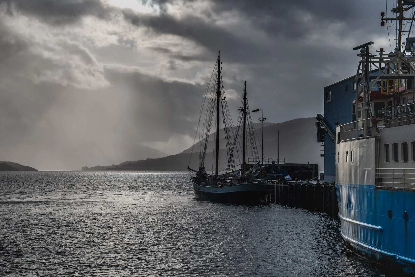 A boat docked at a pier on a cloudy day with mountains in the background.