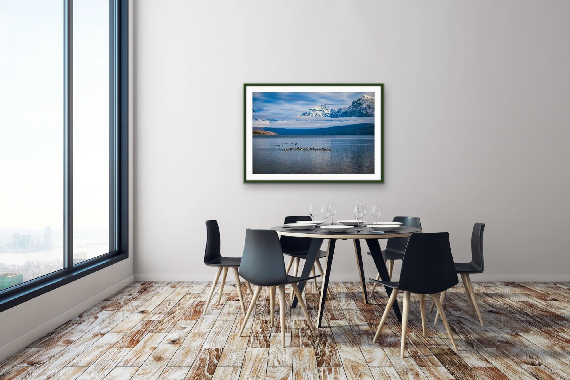 Modern dining room with a round table, six black chairs with wooden legs, set with white plates and wine glasses. Large window on the left with a city view, abstract mountain and lake painting on a white wall.