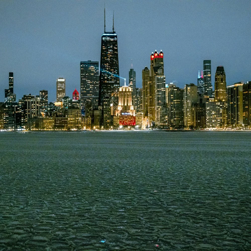 Nighttime city skyline of Chicago viewed from frozen Lake Michigan with illuminated skyscrapers and pancake ice