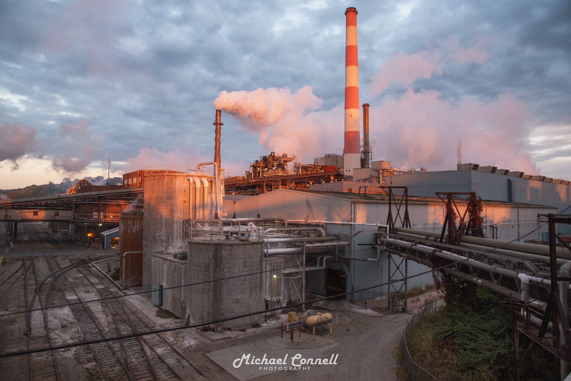 Industrial factory with smokestacks emitting smoke during sunset or sunrise.