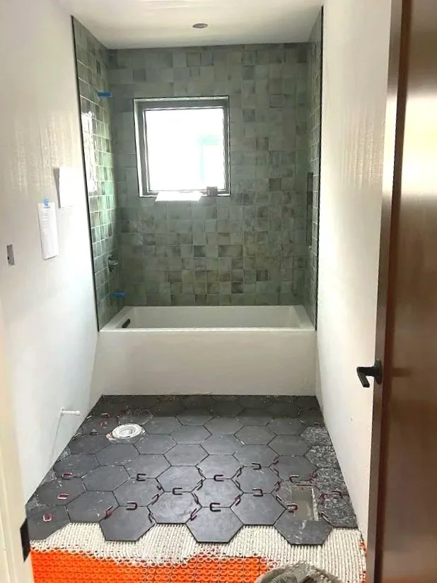 Bathroom under renovation with partially tiled shower area and hexagonal floor tiles being installed.