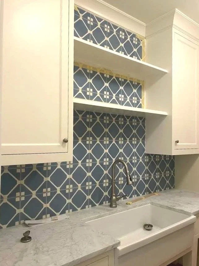 Kitchen backsplash with blue patterned tiles, white cabinets, and a white marble countertop with an under-mount sink.