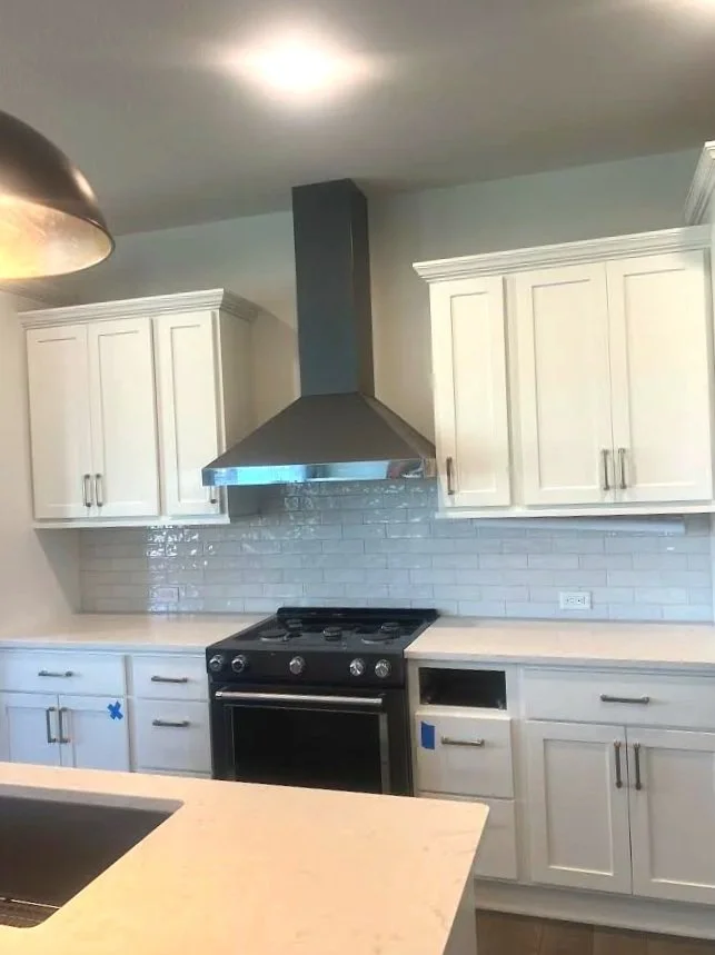 Kitchen with white cabinets, a black stove, gray backsplash, a stainless steel range hood, and a light-colored countertop.