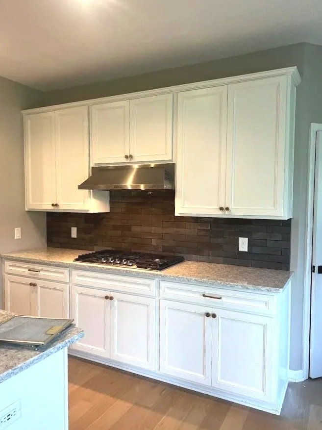 Kitchen with white cabinets, granite countertops, dark brown tile backsplash, stainless steel range hood, and gas stove.