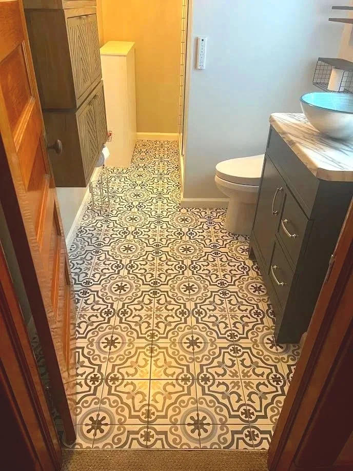 Bathroom with patterned black and white floor tiles, dark vanity with a vessel sink, toilet, gray storage cabinet, and a beige wall.