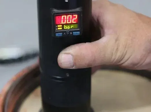 Close-up of a hand holding a digital moisture meter, displaying a reading of 0.02, touching a wooden surface.