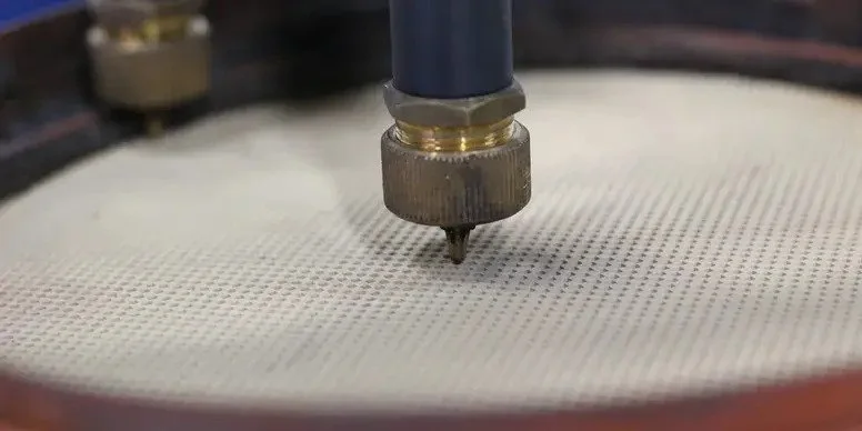 Close-up of a CNC machine tool drilling into a circular white surface.