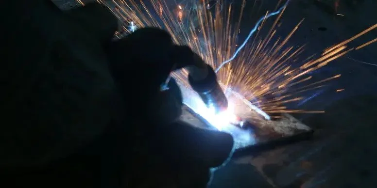 A person performing welding, with sparks flying around as they work on a metal surface.