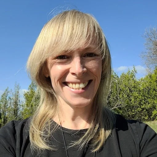 Close up of blonde woman smiling at camera with blue sky and bush background