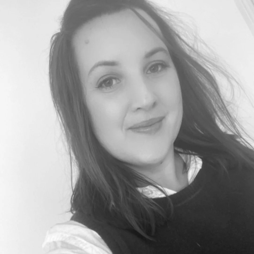 Black and white close-up photo of a woman with shoulder-length hair, smiling gently at the camera, wearing a dark sweater over a light-colored shirt.