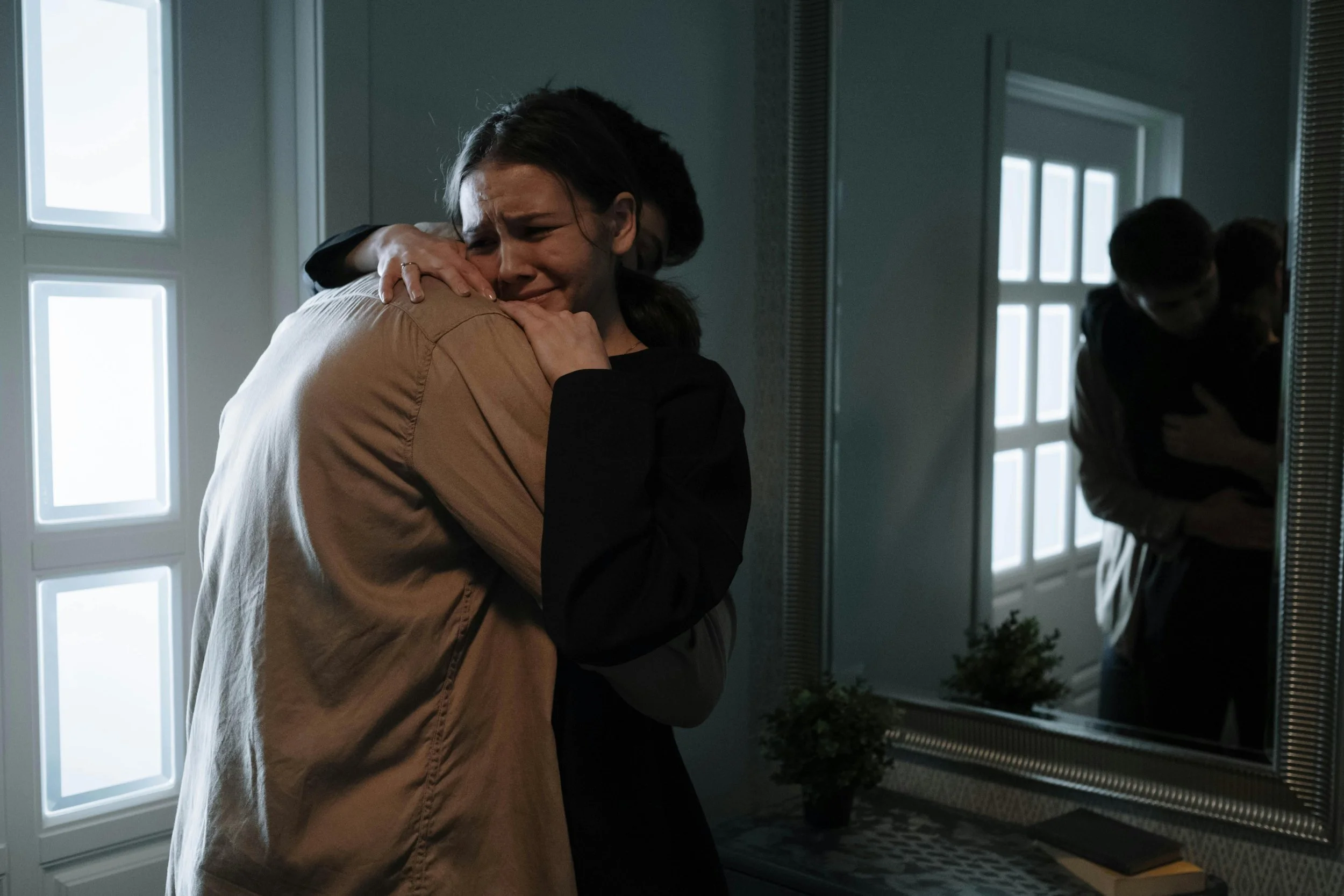 A woman is crying and hugging a man in a bathroom, with a mirror reflecting their embrace.