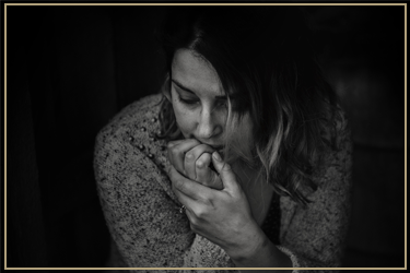 A woman with shoulder-length hair and a patterned sweater, holding her hand near her mouth and appearing pensive.
