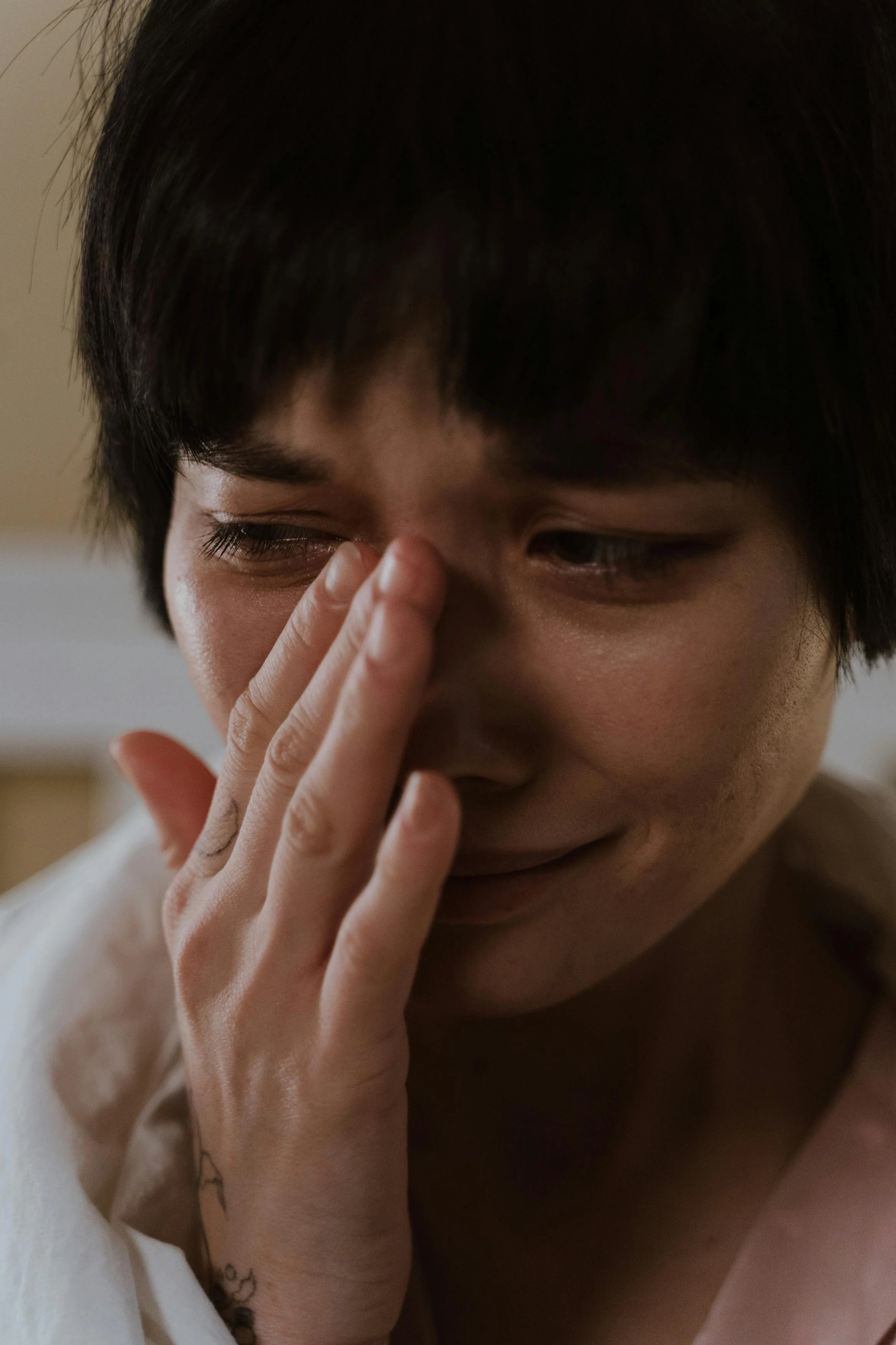 A woman with short dark hair touching her nose with her hand, showing emotional distress.