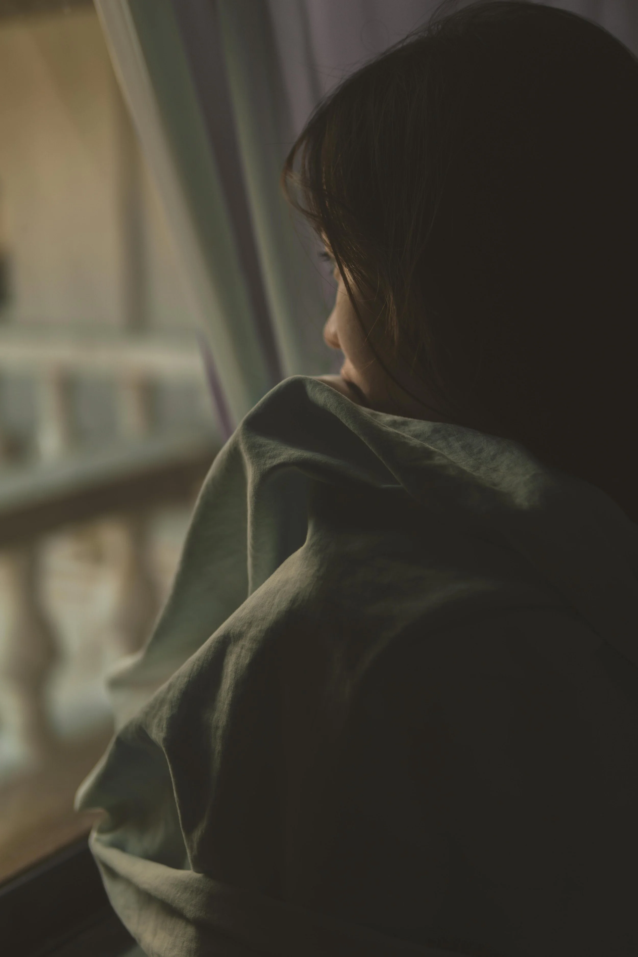 A woman with dark hair looking out a window during daytime.
