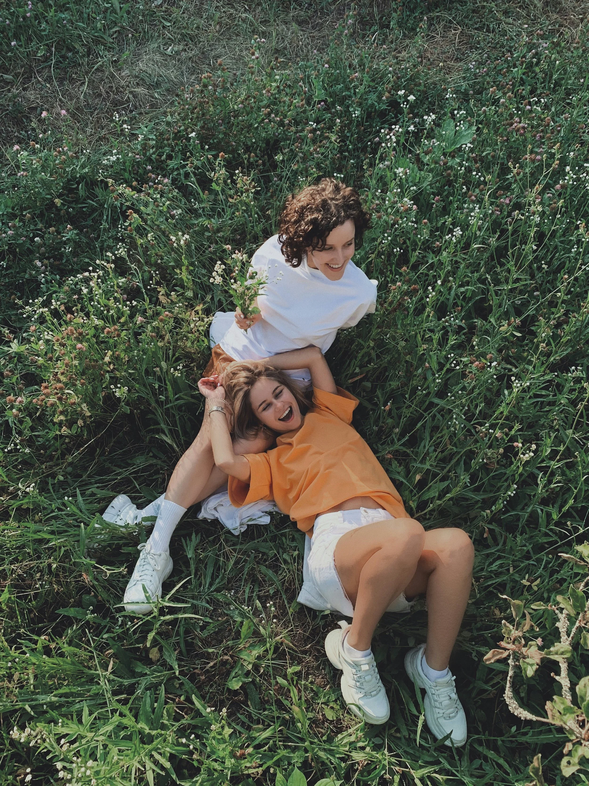 Two women lying in a grassy field with flowers, smiling and relaxed.