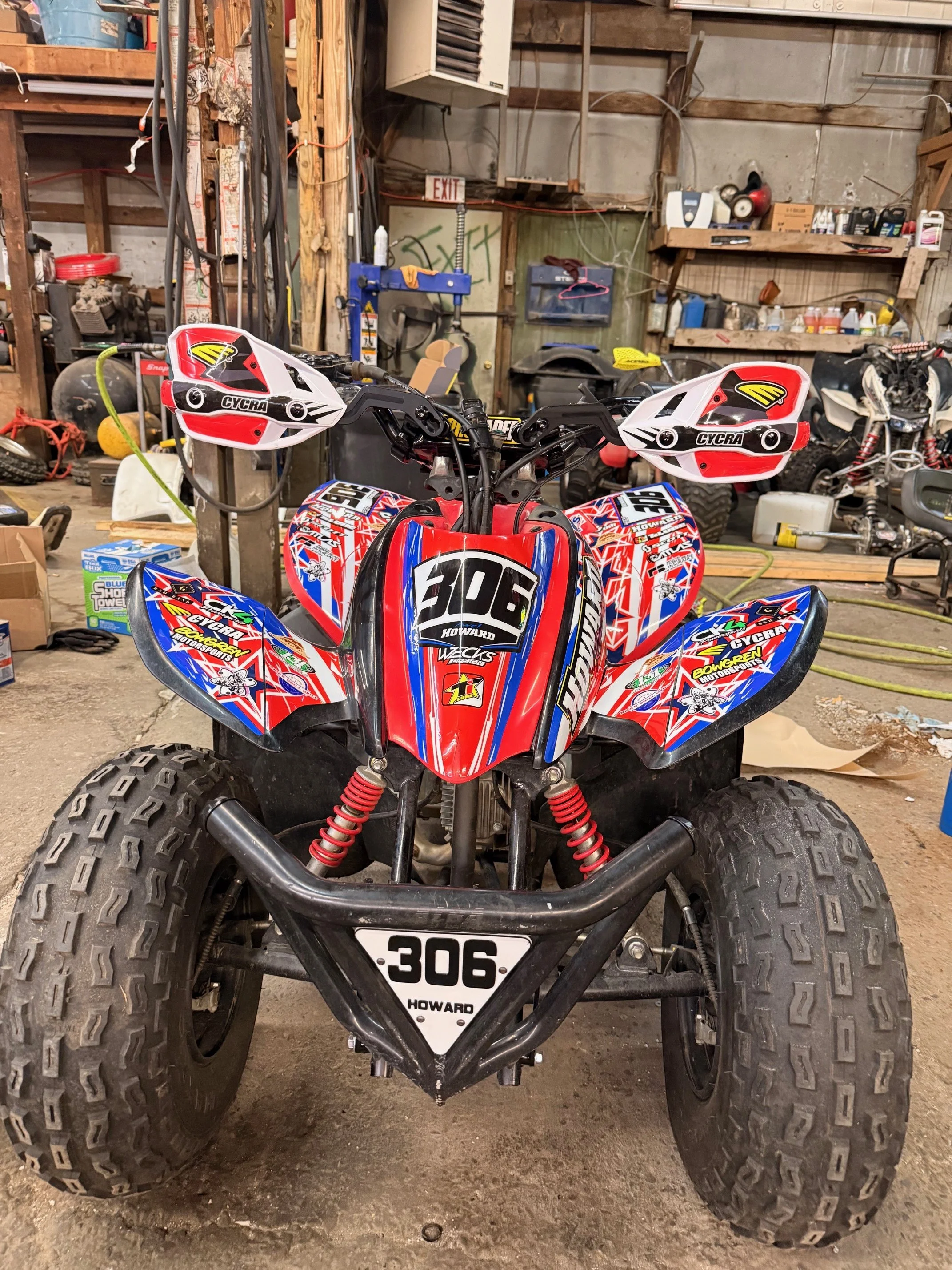 Red, white, and blue sport ATV with racing graphics parked in a cluttered garage