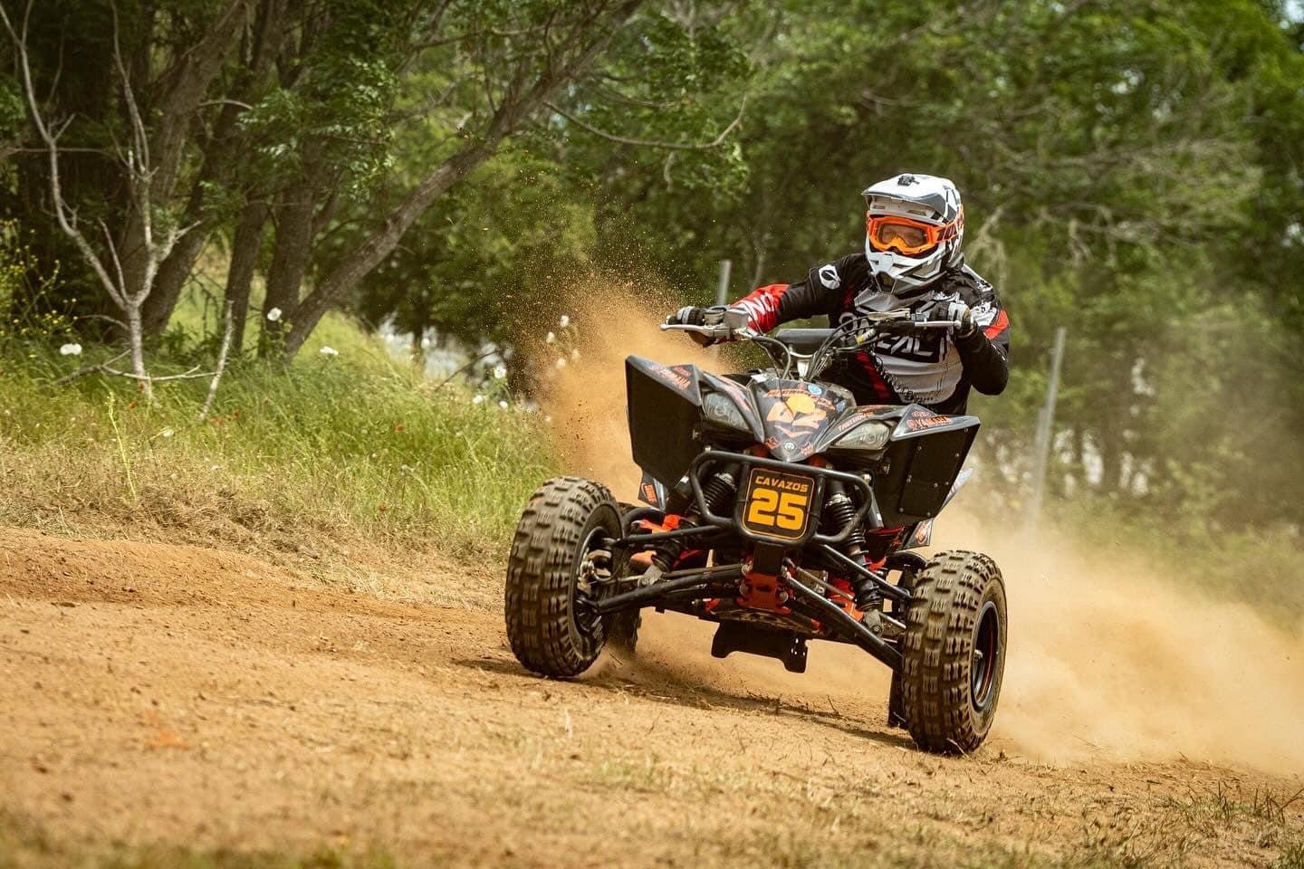 Helmeted rider driving a sport ATV marked number 25 on a dusty forest trail