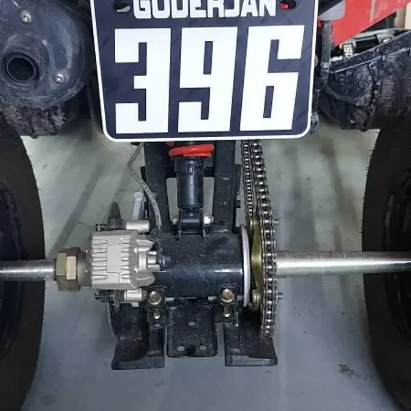 Close-up of an ATV rear axle, chain, sprocket, and differential beneath a custom number plate