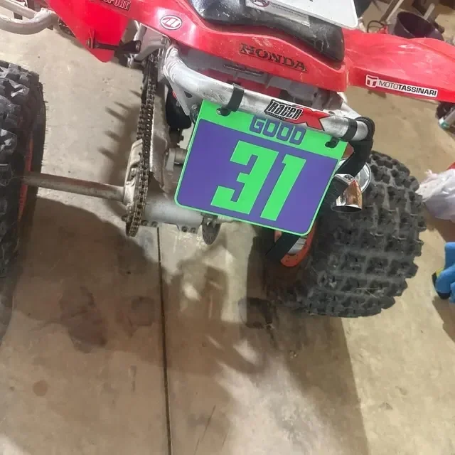Rear view of a red Honda ATV with a green and purple number 31 number plate in a garage