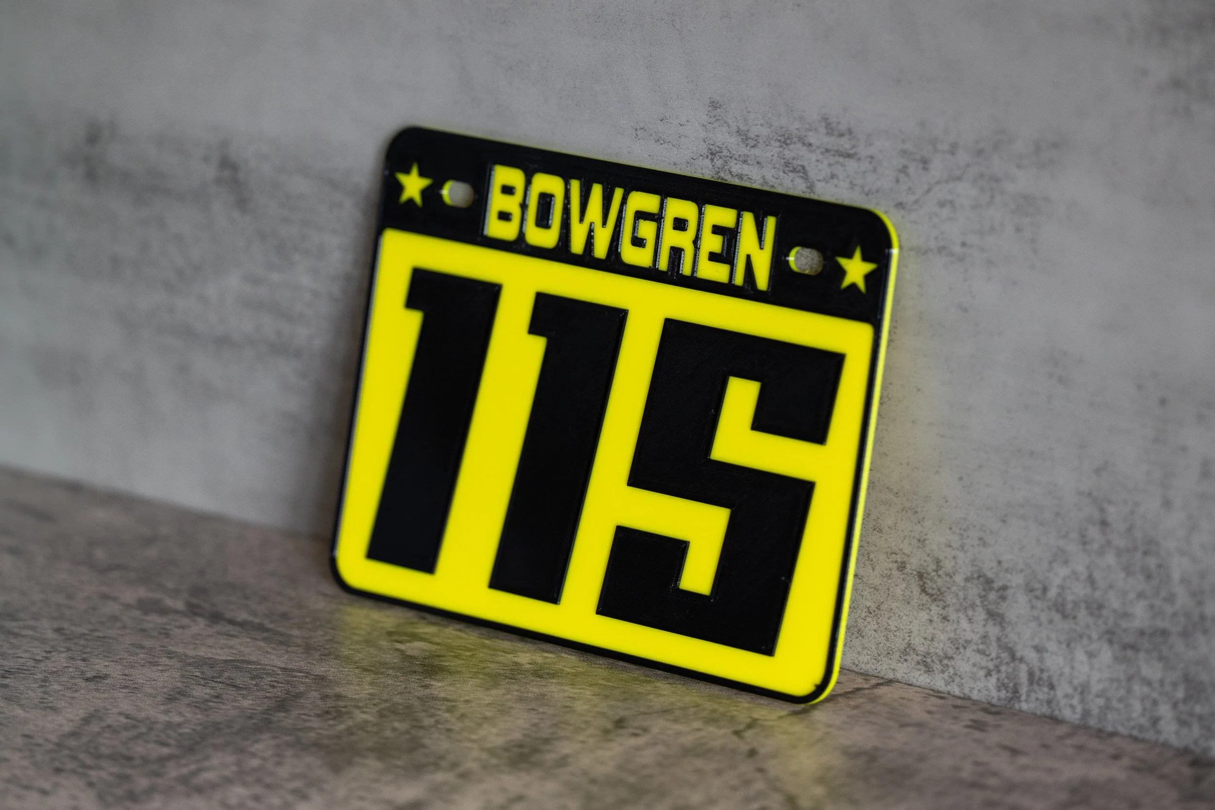 Close-up of a yellow and black European-style license plate reading “BOVGREN” and “T15,” leaning against a gray wall.