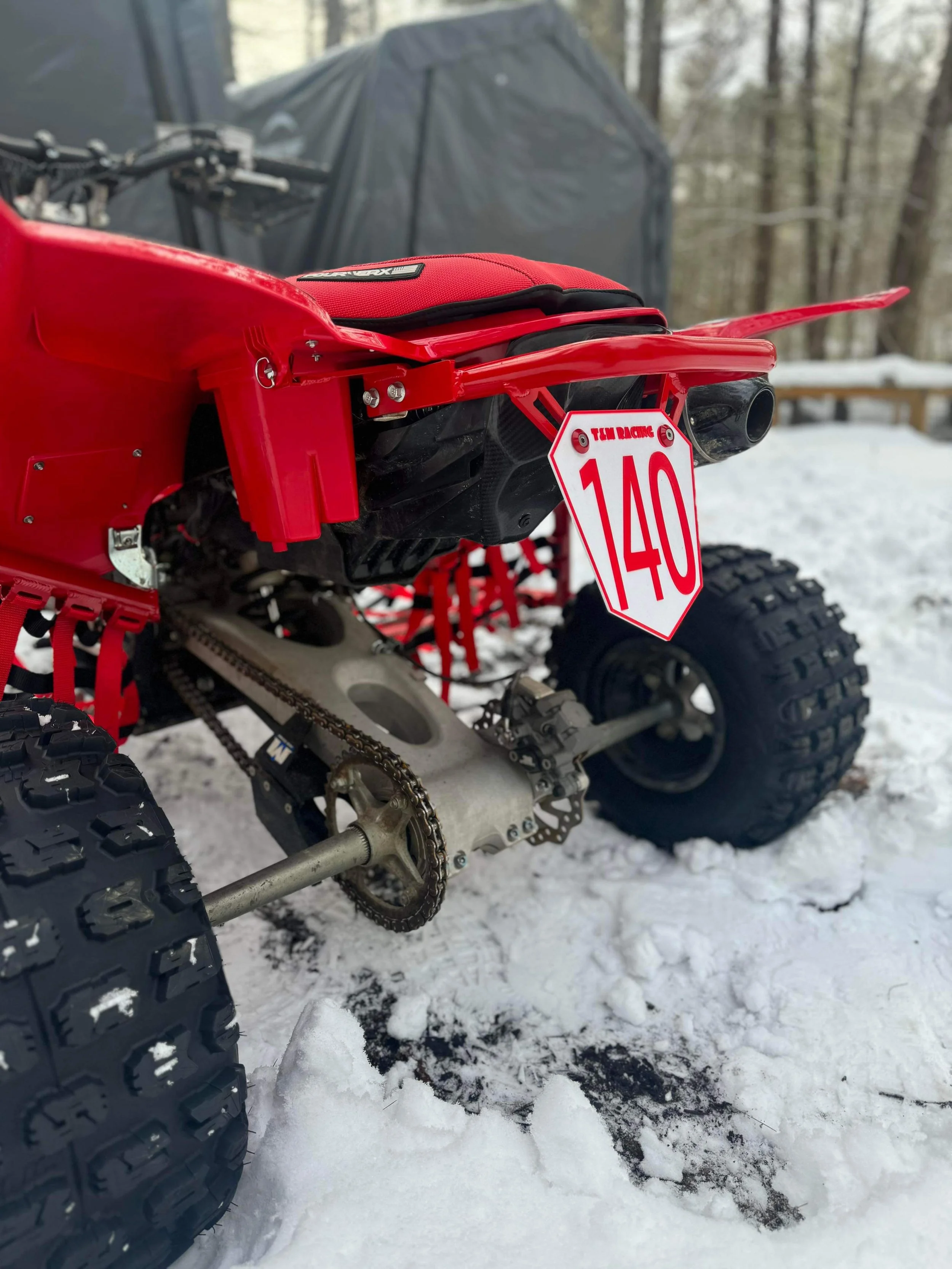 Close-up of a red ATV with a racing number plate parked in snowy woods