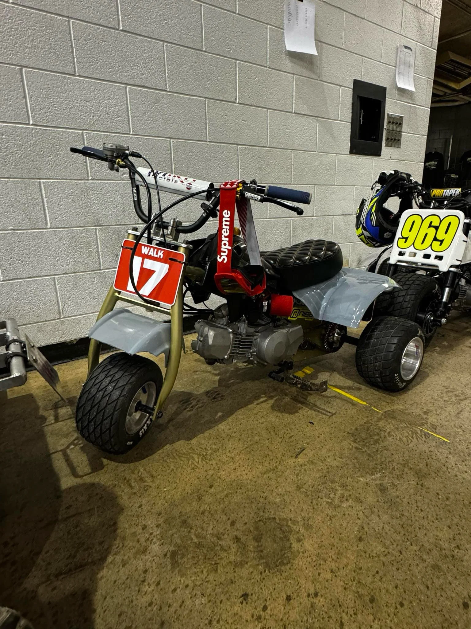 Two customized racing ATVs with number plates and helmets parked indoors.