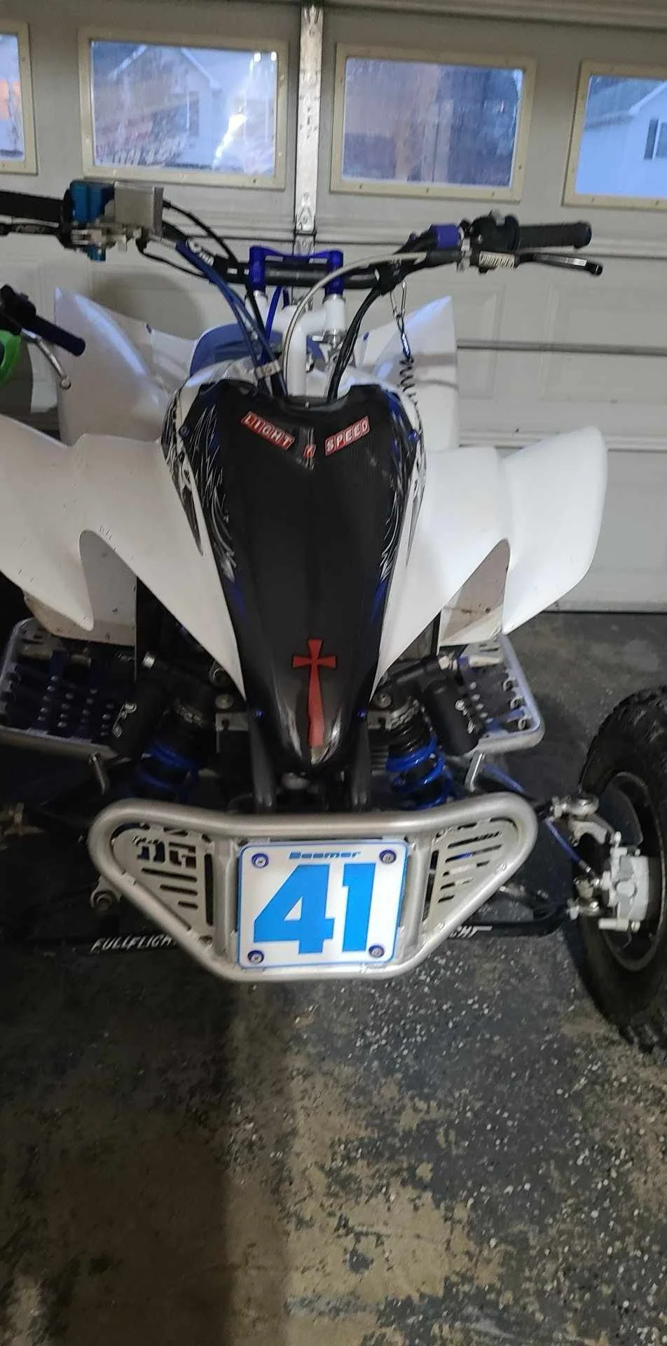 Front view of a blue, white, and black off-road ATV with number 41 plate and custom handguards in a garage