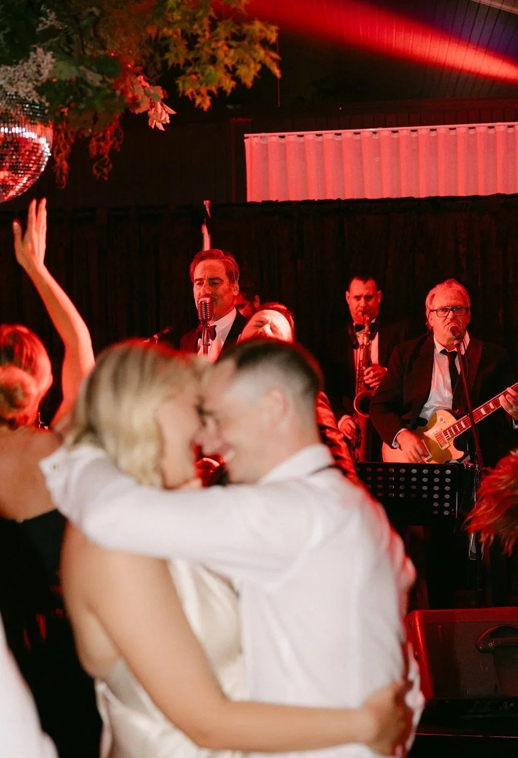 A couple dancing and smiling at a wedding reception with a live band performing in the background.
