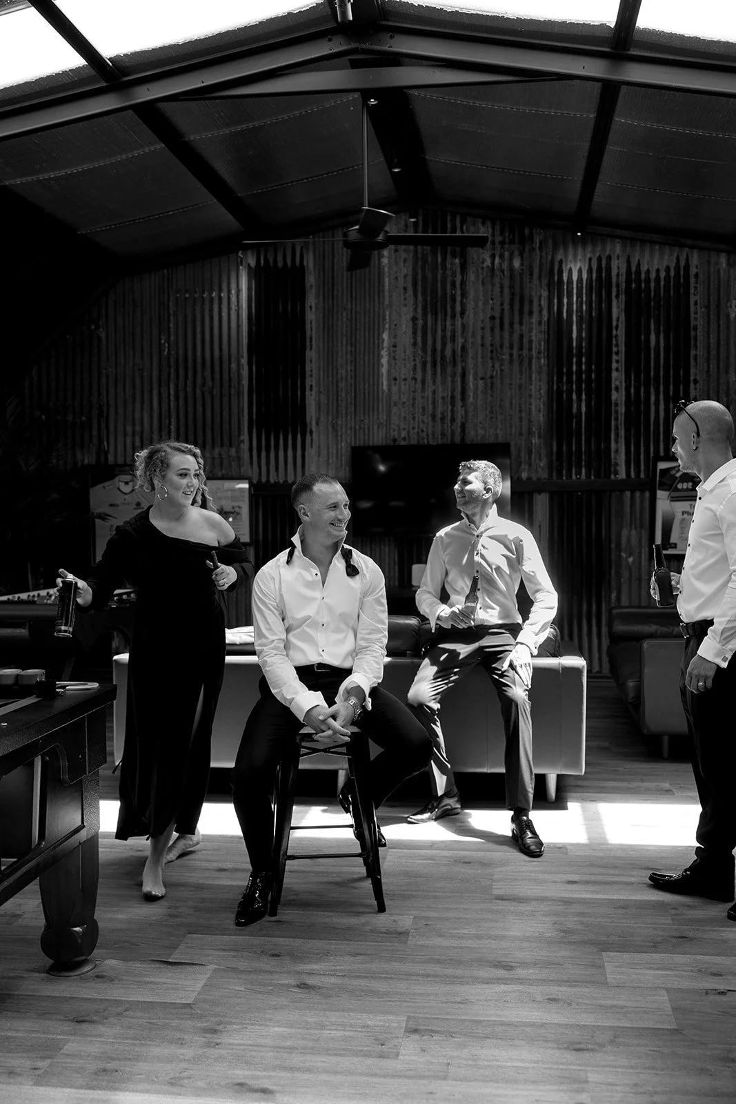 Four people, two women and two men, in a social setting, smiling and holding drinks, with a pool table and television in the background.