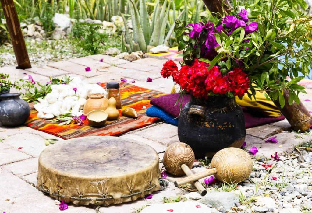 Outdoor scene with a drum, colorful cloth, vases, flowers, and musical instruments on a stone surface