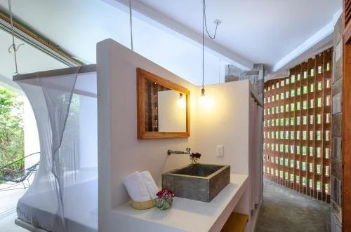 Bathroom with concrete sink, wooden framed mirror, hanging pendant light, white towels, and decorative flowers.