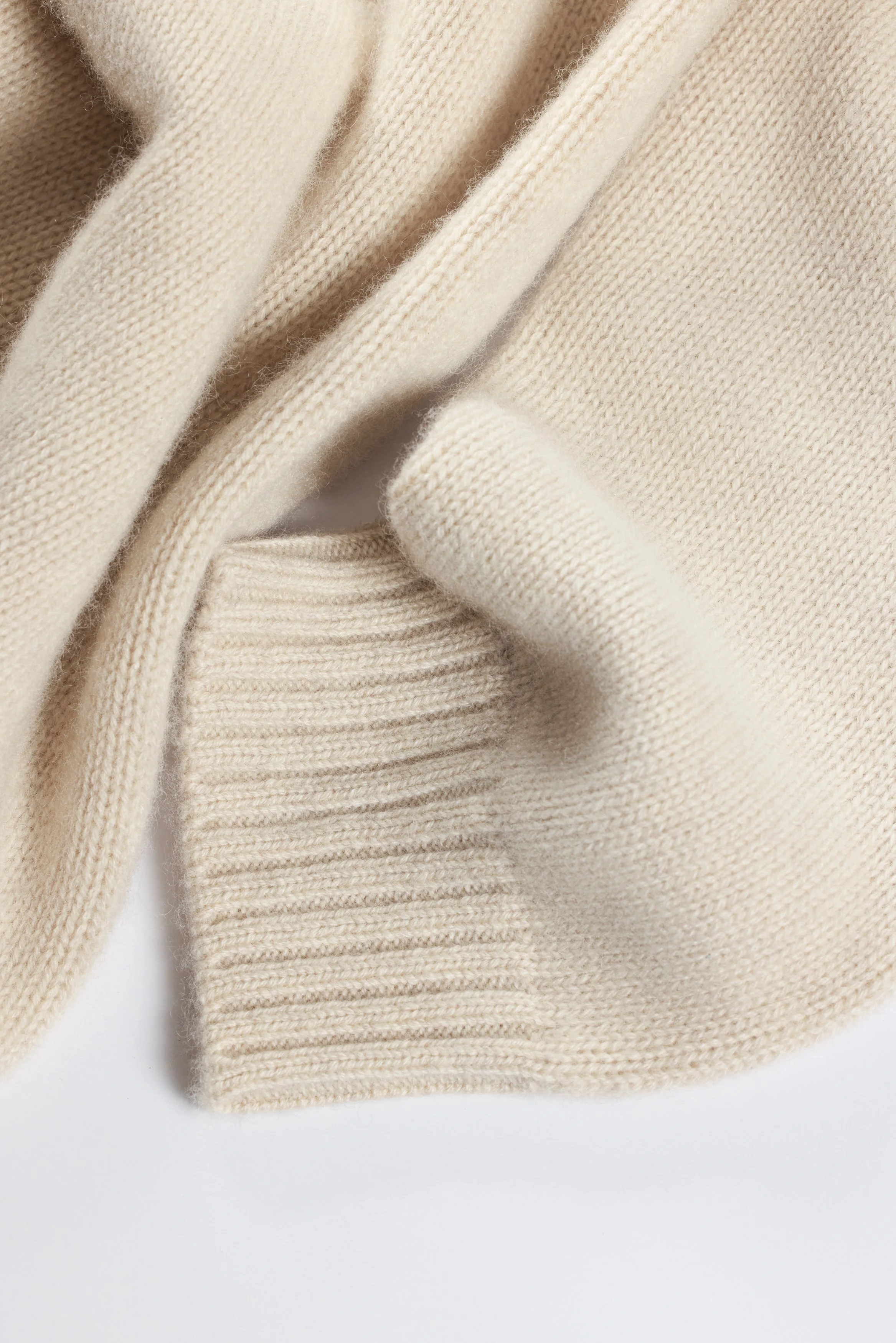 Close-up of three cream-colored sweaters, showing textures and fabric details.