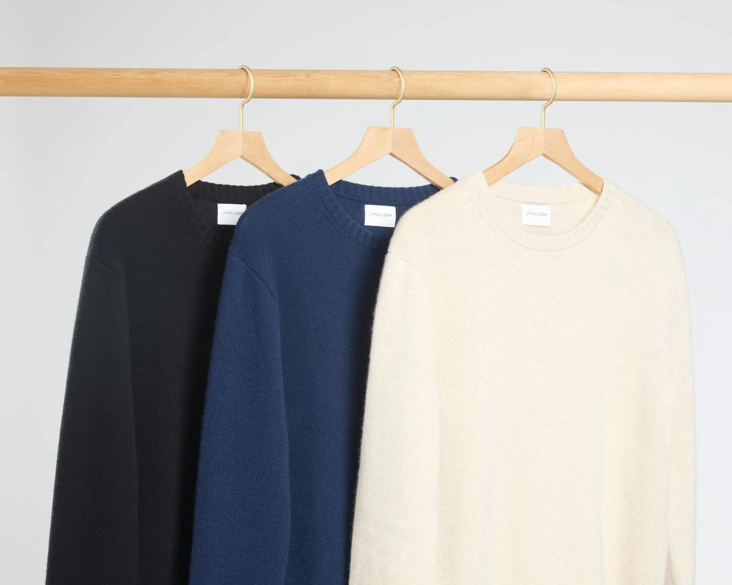3 cashmere sweaters hanging on a wood pole.