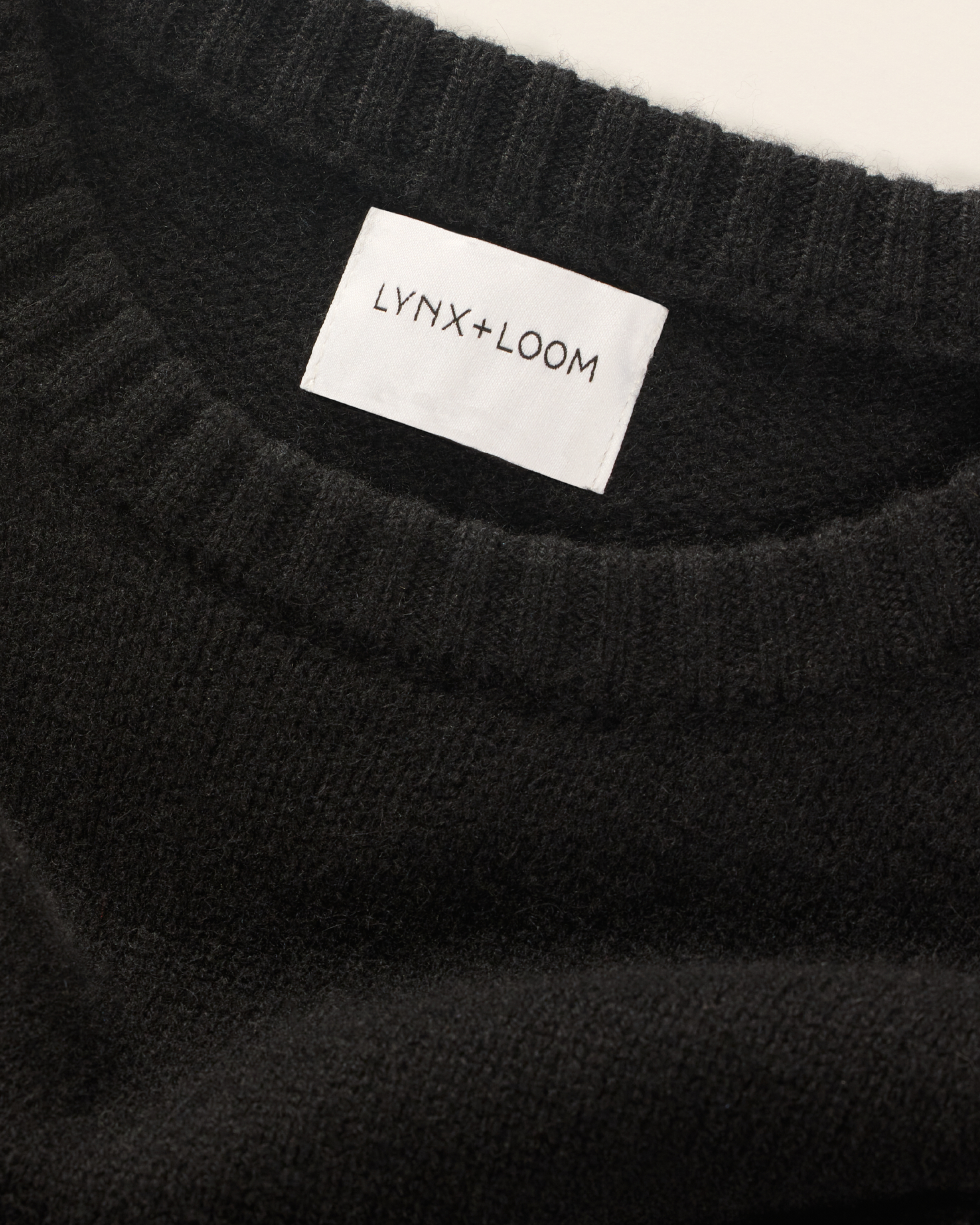 Close-up of a black knit sweater with a white label that reads 'LYNX+LOOM' stitched inside the collar.