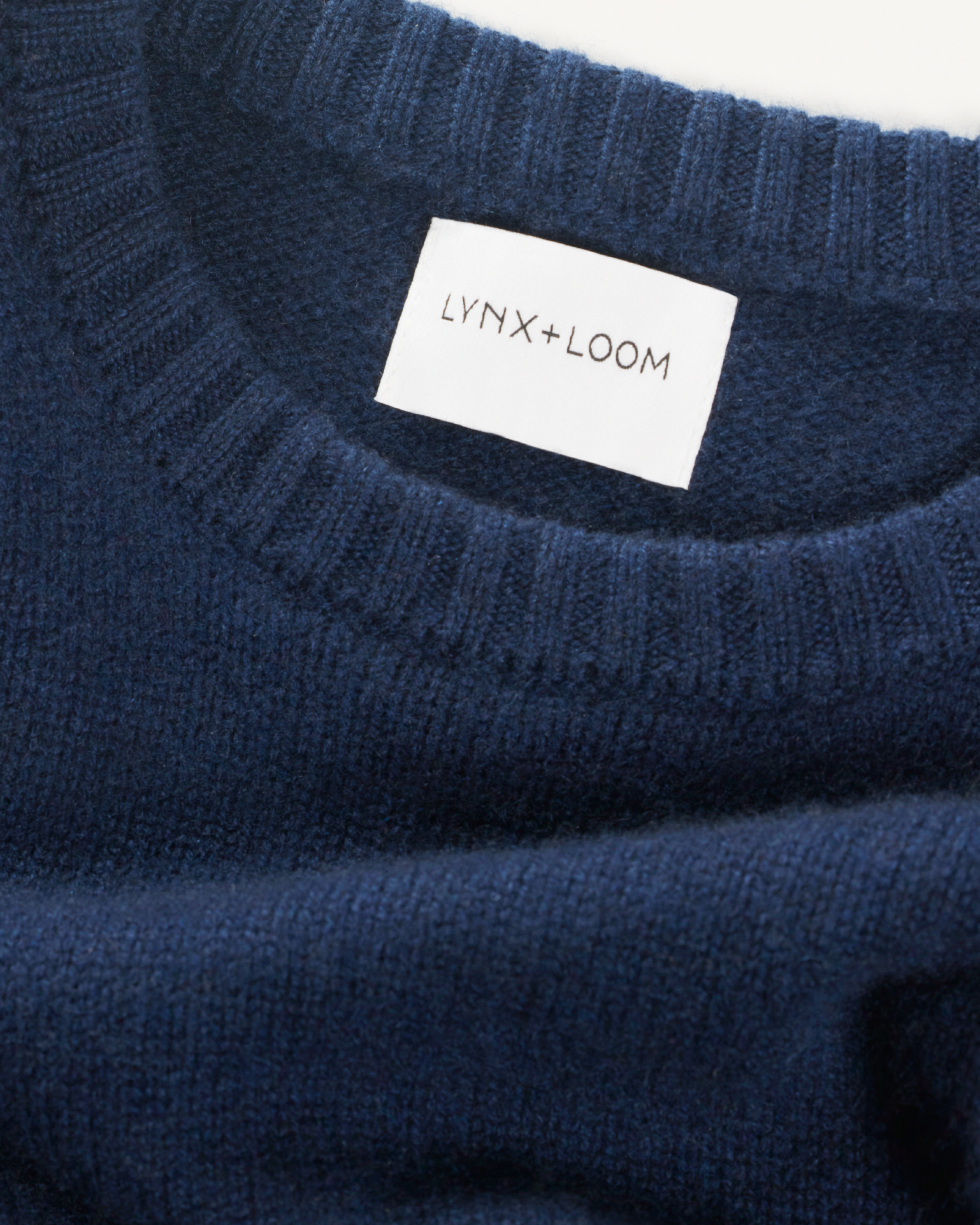 Close-up of a navy blue Knit+Loom sweater with a white label inside that reads "LYNX+LOOM".