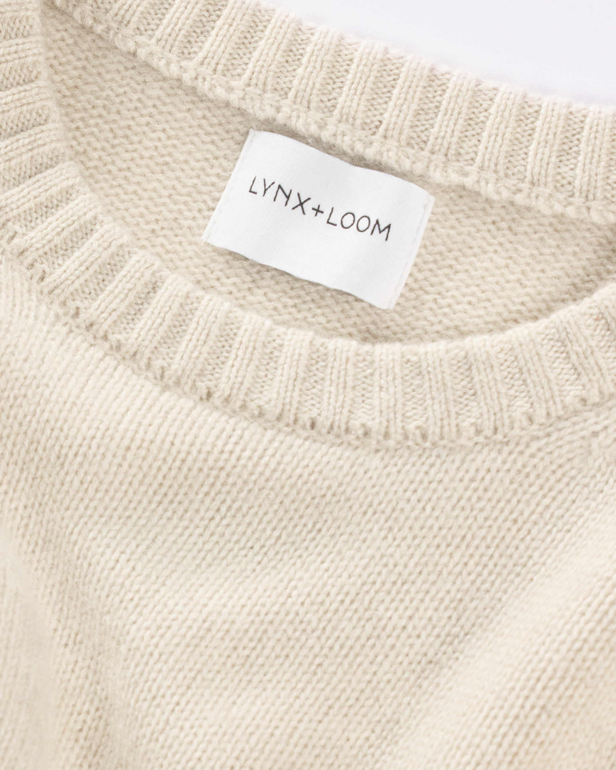Close-up of a cream-colored knitted sweater with a "LYNX+LOOM" label.